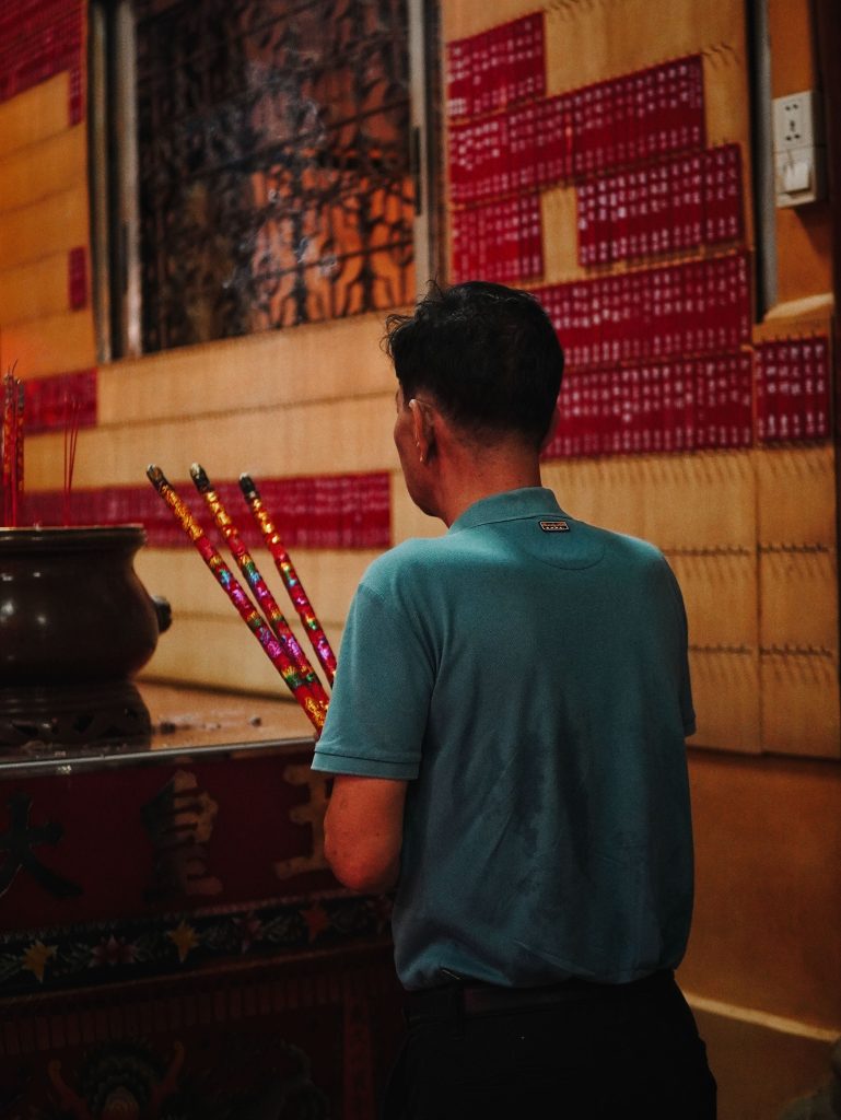 Man holding incense sticks in a tranquil Asian temple, capturing a moment of prayer and reflection.