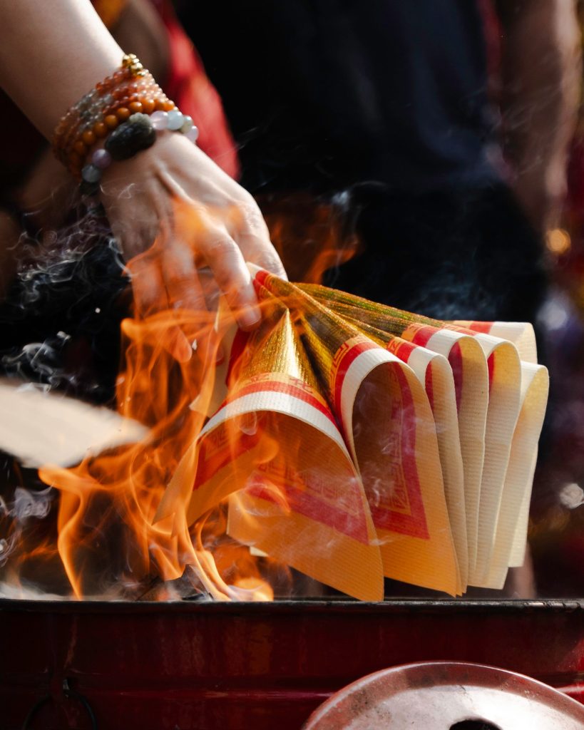A hand burning colorful joss paper in a traditional religious ceremony.